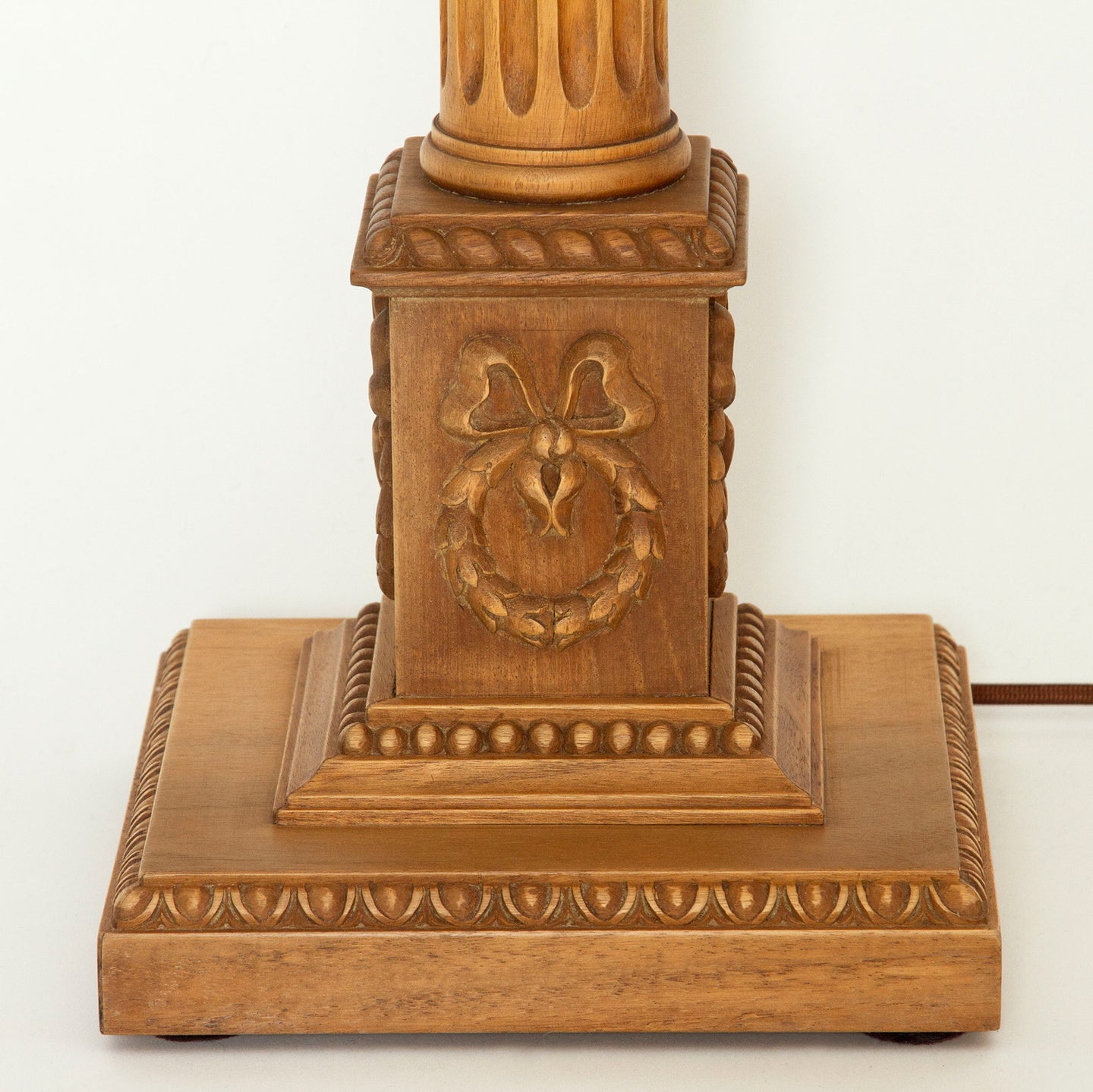 Close-up of the wooden columnar lamp’s base, showcasing detailed carvings, including a wreath, bow, and egg-and-dart trim.