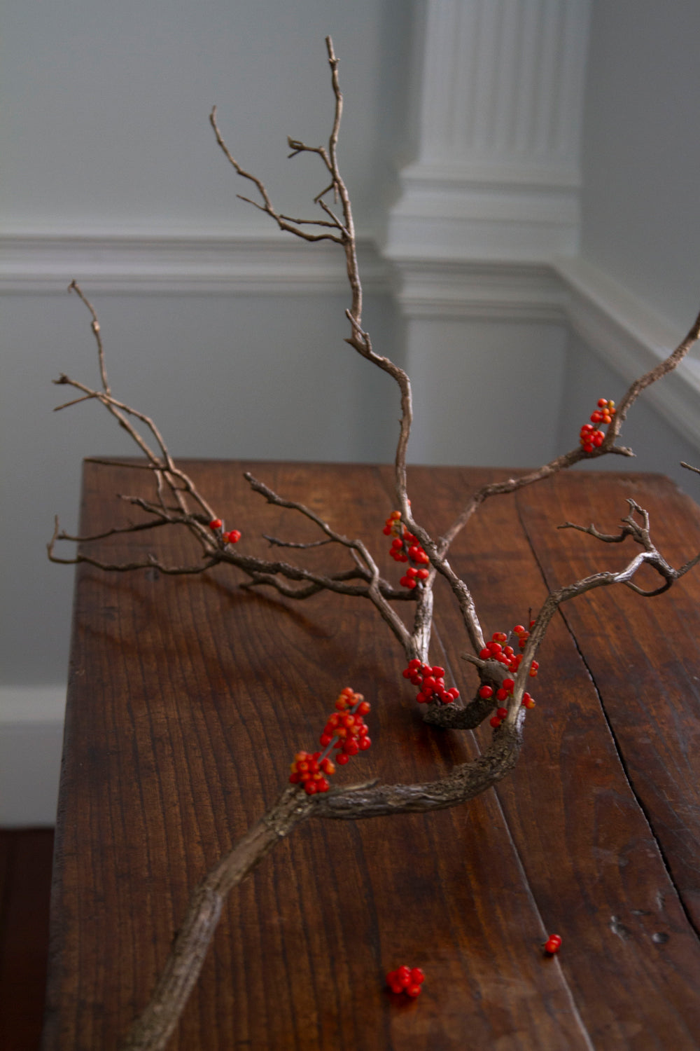 Sculptural bronze branch bud vase holding red berries, with Ikebana-inspired design.