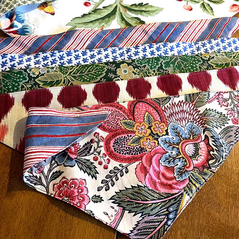 Stack of reversible dog bandana made from designer fabrics, available in small, medium, and large sizes with tie closure.