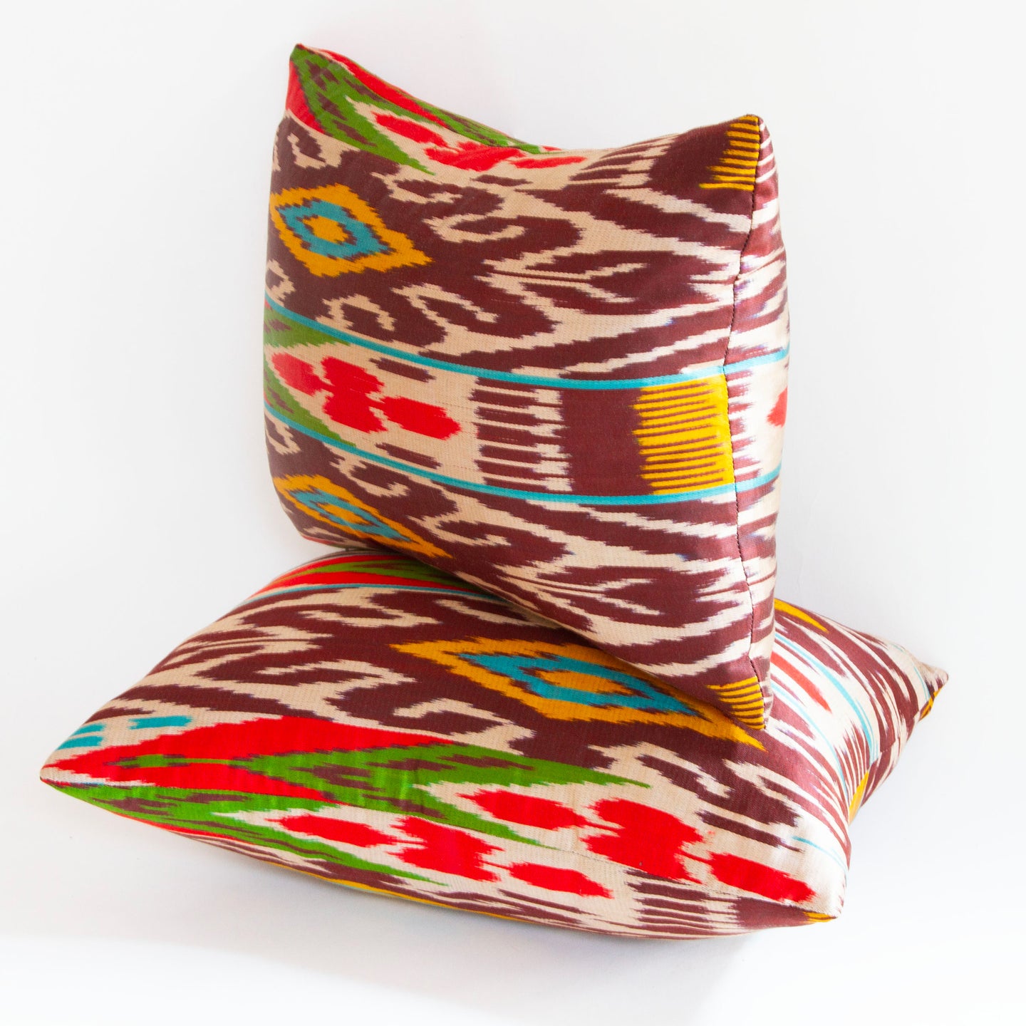 Multicolored silk ikat pillows in magenta, saffron, aubergine, and green on ecru. Size: 13” x 18”.