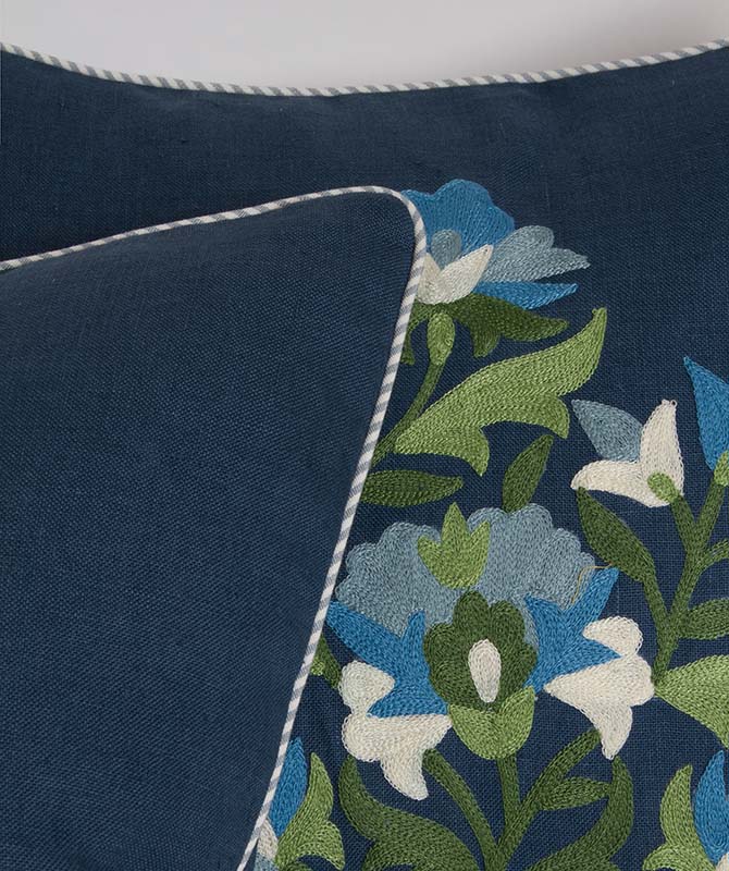 Striped welt detail on pillow with vibrant green and blue embroidery on navy linen, bias-cut.