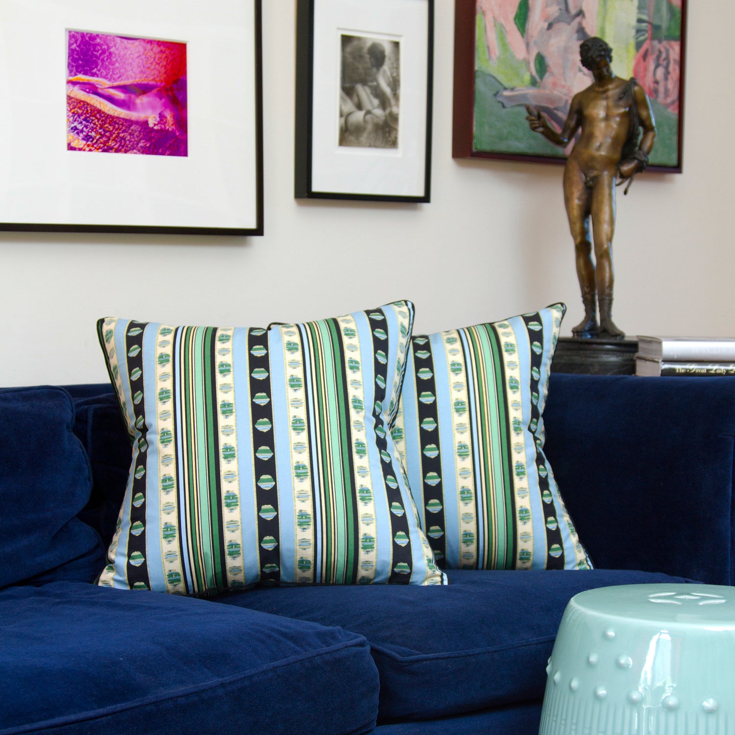 Rayure Cachemire pillows with blue, green, and black stripes contrast against a deep blue couch, highlighting the bold design and black braided cord trim.