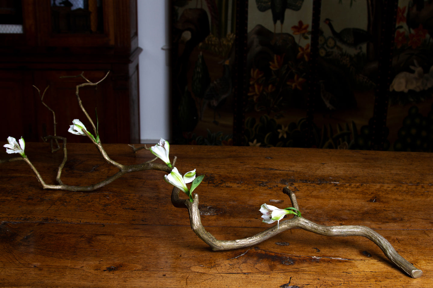 Bronze branch bud vase with tiny water holes holding white flowers, inspired by Ikebana,.