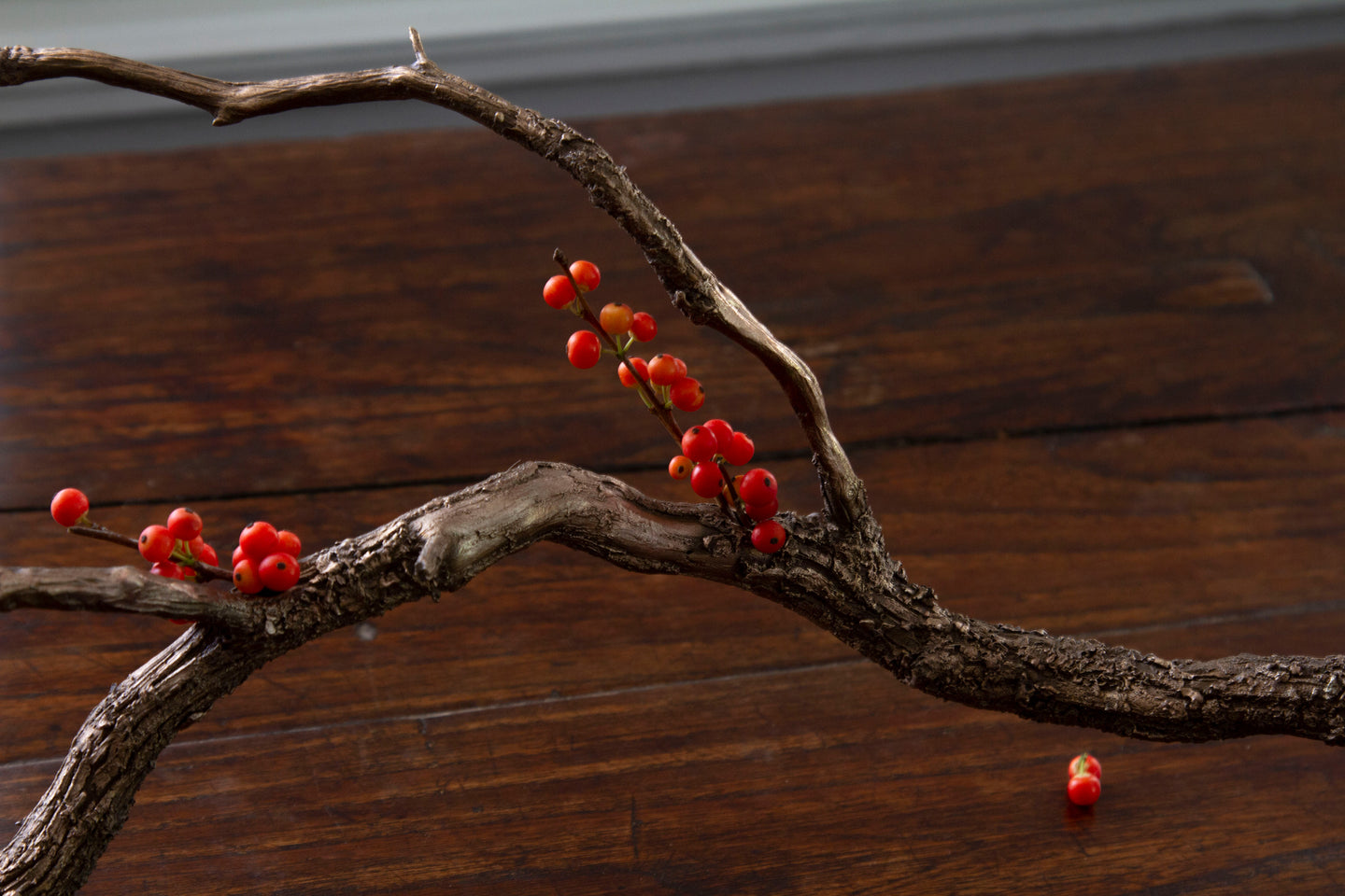 Sculptural bronze branch bud vase holding red berries, with Ikebana-inspired design.