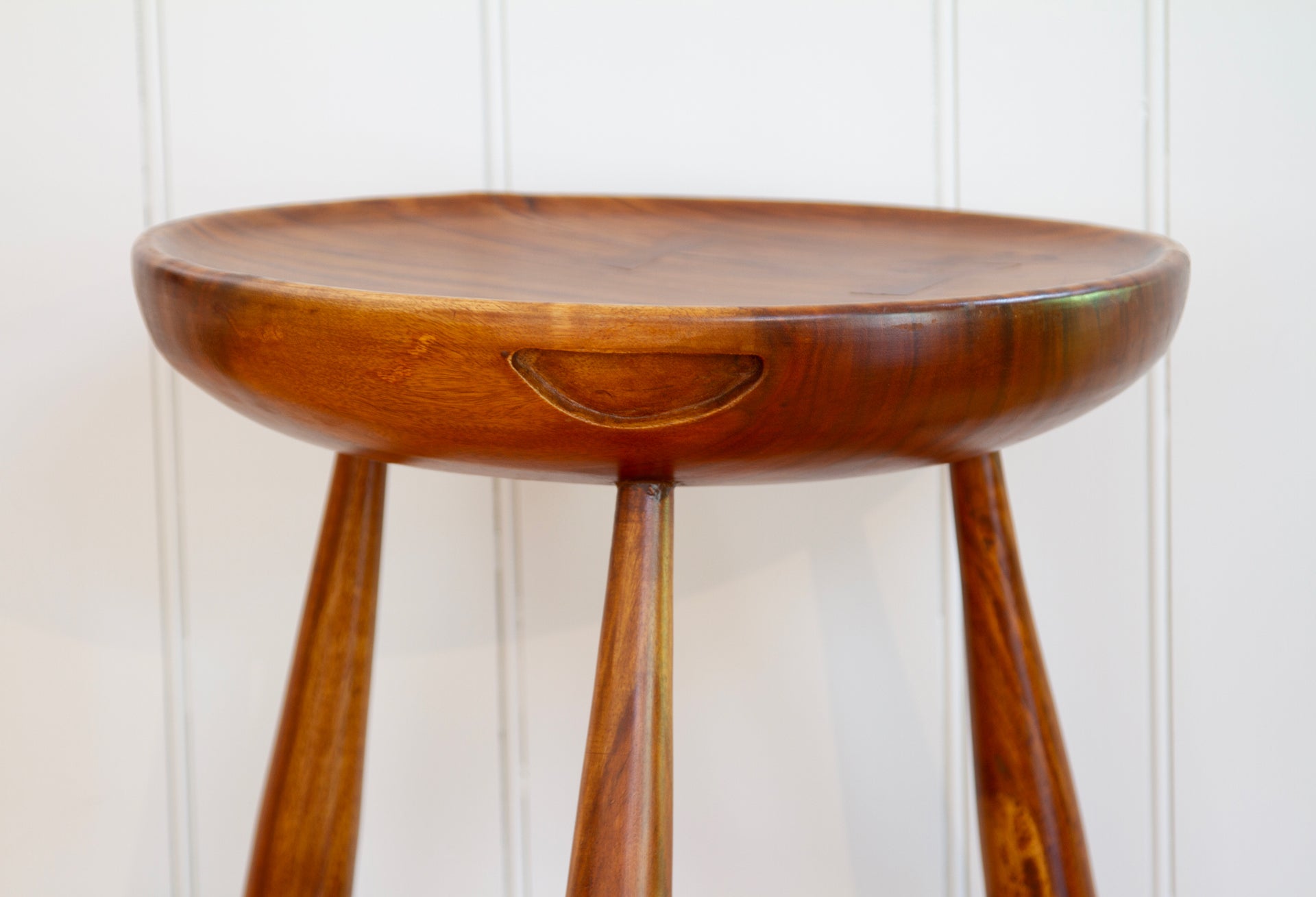 Top detail on walnut three-legged stool with carved handles and concave tops.  Used as side tables or seating.