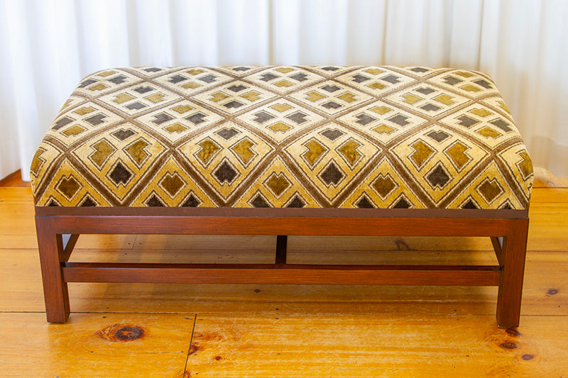 Ottoman upholstered in sand and cognac Kuba cloth epingle velvet with espresso trim, measuring 42”W x 24”D x 17”H.