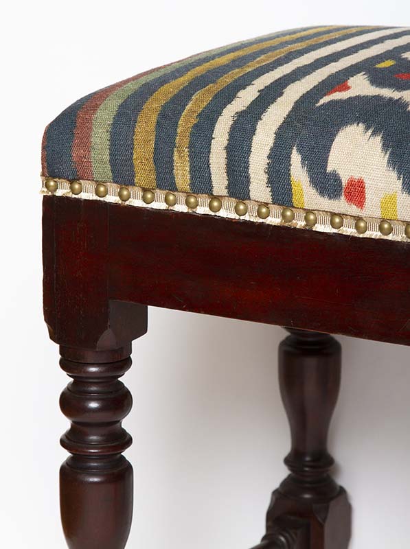 Caster detail on antique mahogany stool upholstered in Pierre Frey’s Caracus in Sangria with silk gimp trim. 24”W x 17”D x 23”H.